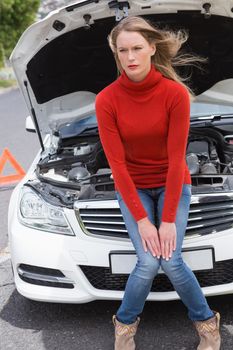 Annoyed young woman beside her broken down car in the street 