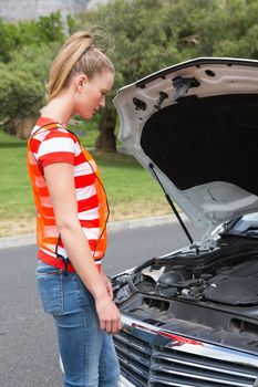 Worried young woman beside her broken down car in the street