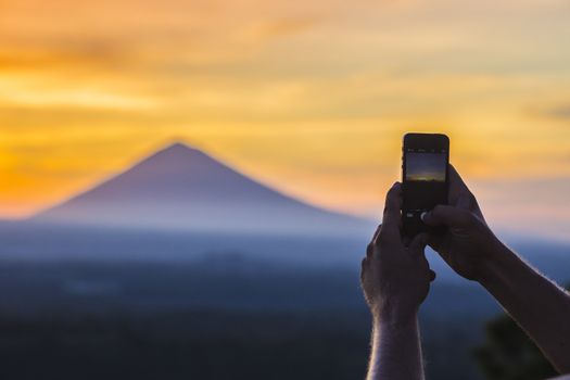 Man with Mobile Phone and Volcano Agung as Background.at Sunrise Time,Bali,Indonesia.