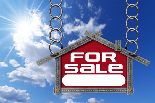 Grey metallic meter ruler in the shape of house with text for sale. For sale real estate sign on blue sky with clouds and sun rays