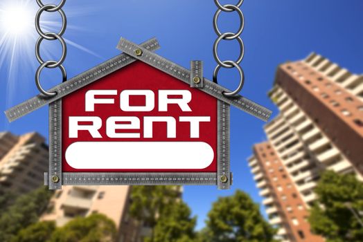 Grey metallic meter ruler in the shape of house with text for rent. For rent real estate sign with tall and blurred buildings in the background