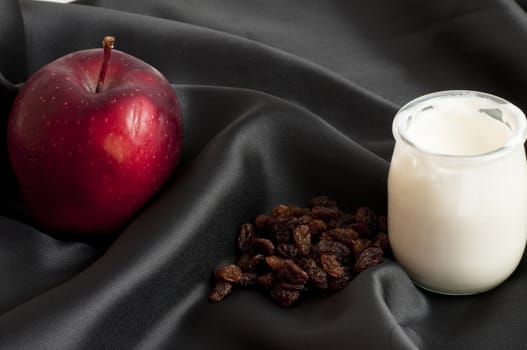 white yoghurt in a bowl on a sheet of black silk with close blueberries and apple