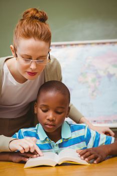 Portrait of teacher assisting little boy with homework in the classroom