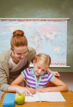 Portrait of teacher assisting little girl with homework in the classroom