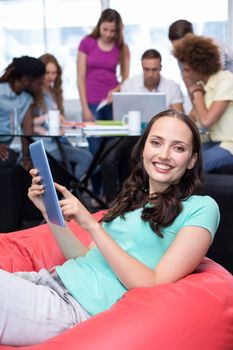 Smiling female student using digital tablet with friends in background