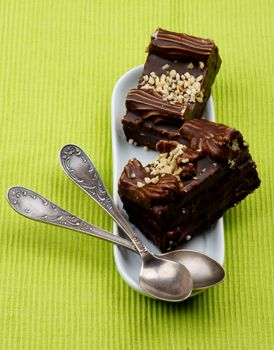 Chocolate Mocha Cakes Mocha Frosting, Cream and Nuts on White Dessert Plate with Silver Tea Spoons closeup on Green Textile background