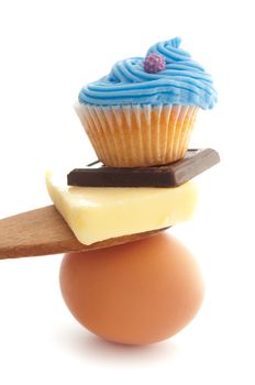 Baking foods balanced on top of each other including chocolate, butter, egg and cupcake