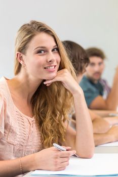 Portrait of smiling female student writing notes in classroom