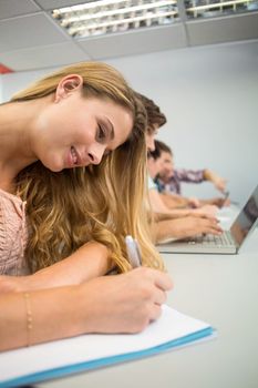 Side view of students writing notes in classroom