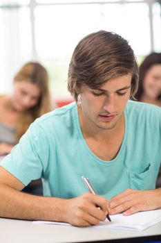 Portrait of male student writing notes in classroom