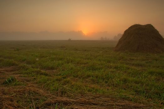 Poland,late summer.Dawn above meadows in the vicinity of the Narew river.On the foreground the one can see the mound of the cut grass and in the background of the fog and the glow of the rising sun.Horizontal view.