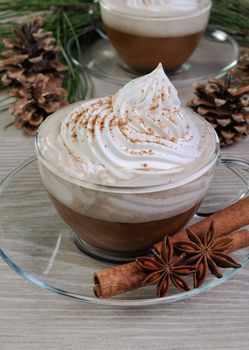 Cup of coffee with whipped cream and cinnamon on the table with pine cones