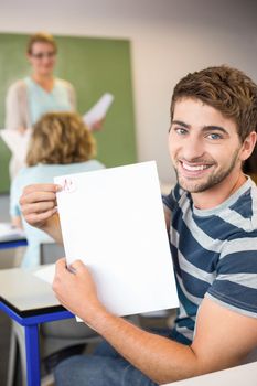 Portrait of happy male student holding paper in the class