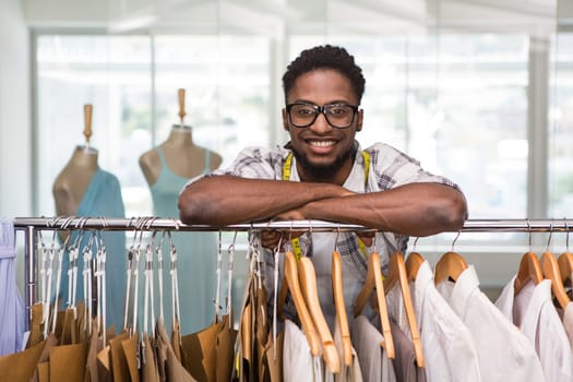 Portrait of male fashion designer leaning on rack of clothes