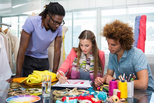 Team of young fashion designers sketching at table