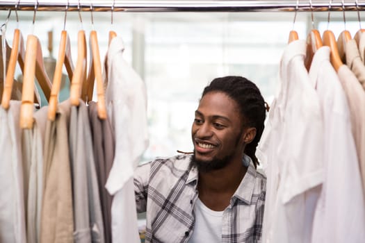 Portrait of male fashion designer looking at rack of clothes