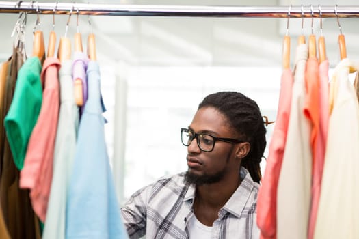 Portrait of male fashion designer looking at rack of clothes