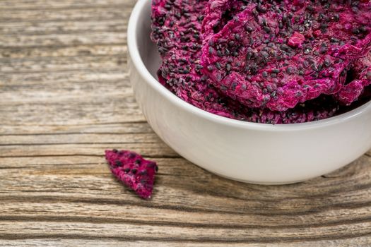 slices of dried red dragon fruit in a white, ceramic bowl against grained wood