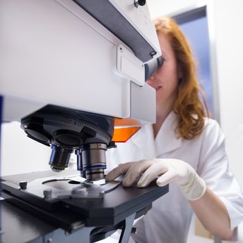 Female scientist microscoping on hi-tec fluorescent microscope. . Health care professional in hes working environment.