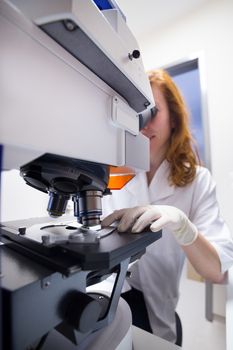 Female scientist microscoping on hi-tec fluorescent microscope. . Health care professional in hes working environment.