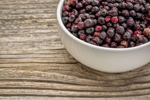 freeze dried elderberries in white, ceramic bowl against grained wood