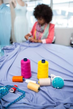 Close up of threads on table with female fashion designer in background