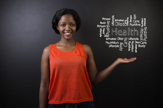 South African or African American woman teacher or student with her hand out standing against a blackboard background with a chalk health diagram