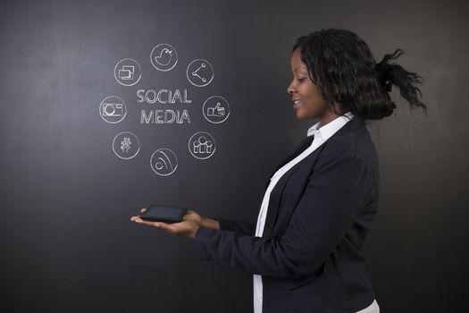 South African or African American woman teacher or student holding tablet computer showing social media chalk concept on a blackboard background