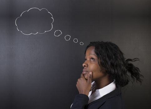 South African or African American woman teacher or student standing against blackboard background thinking with chalk thought clouds