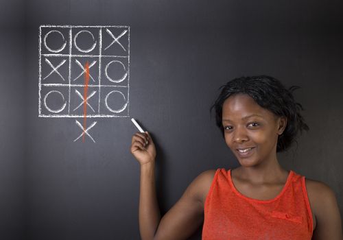 Thinking out of the box South African or African American woman teacher or student pointing at a tic tac toe concept on a blackboard background