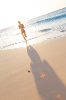 Happy woman enjoying in summer, running joyfully on tropical beach in sunset. Beautiful caucasian model wearing bikini on vacations on sandy beach. Footprints in sand. 
