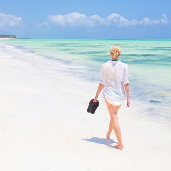 Caucasian woman walking joyfully on tropical beach. Beautiful caucasian model  wearing white beach tunic on vacations walking down picture perfect Paje beach, Zanzibar, Tanzania. Copy space.