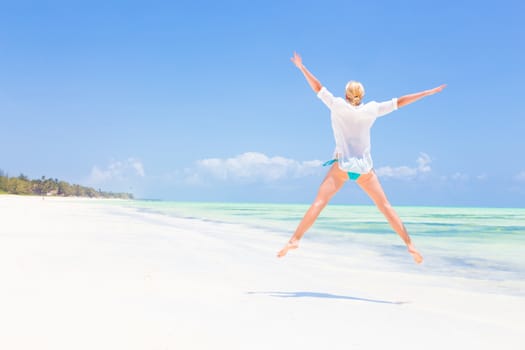 Beautiful Girl Jumping on Beach. Vacation Concept Woman enjoying, relaxing joyfully in summer. Beautiful caucasian model wearing white tunic jumping on picture perfect Paje beach, Zanzibar, Tanzania.