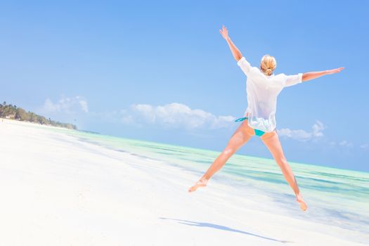 Beautiful Girl Jumping on Beach. Vacation Concept Woman enjoying, relaxing joyfully in summer. Beautiful caucasian model wearing white tunic jumping on picture perfect Paje beach, Zanzibar, Tanzania.