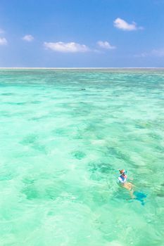 Young woman snorkeling in clear shallow sea of tropical lagoon with turquoise blue water and coral reef,  near exotic island. Mnemba island, Zanzibar, Tanzania.