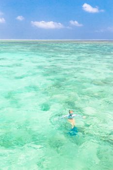 Young woman snorkeling in clear shallow sea of tropical lagoon with turquoise blue water and coral reef,  near exotic island. Mnemba island, Zanzibar, Tanzania.