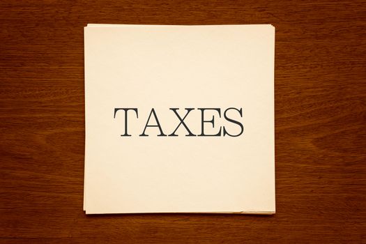 Top view of white paper cards with word " TAXES " putting on natural wood background, vignette and sepia tone image