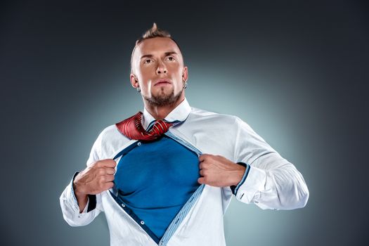 businessman acting like a super hero and tearing his shirt off on a gray background
