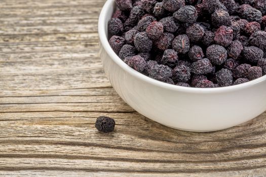 Dried chokeberry (aronia berry) in a small, ceramic bowl against grained wood