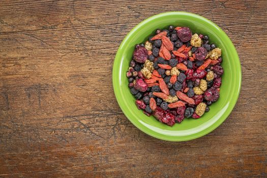 superfruit berry mix (blueberry, mulberry, cherry, goji, elderberry, chokeberry, and cranberry) - green ceramic bowl against grunge wood