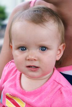 A cute baby girl sits outside in the summertime with her mom.