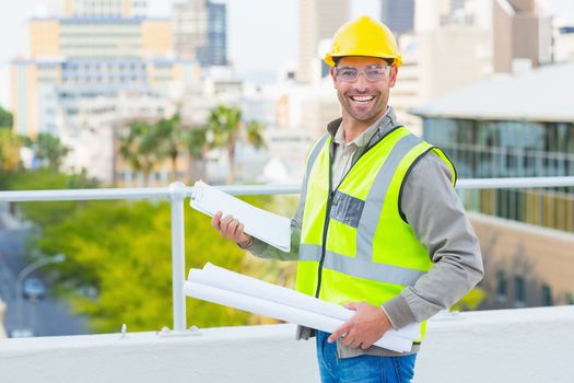 Portrait of smiling male architect with blueprints and clipboard outdoors