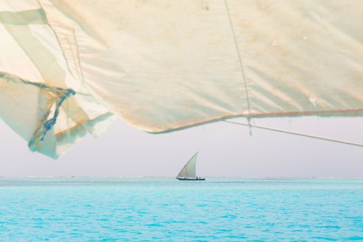 Traditional wooden sailboat sailing on a horizon of turquoise blue sea of Zanzibar, Tanzania, Afrika.