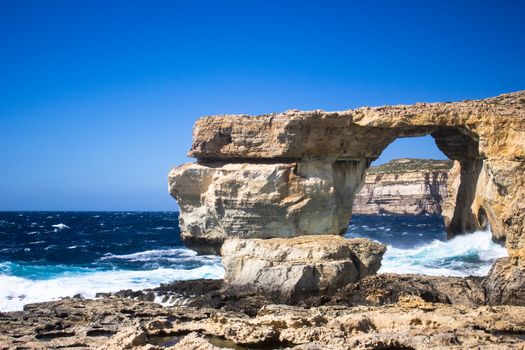 the rugged coastline of the island of Gozo are reflected in a blue sea