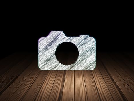Tourism concept: Glowing Photo Camera icon in grunge dark room with Wooden Floor, black background, 3d render