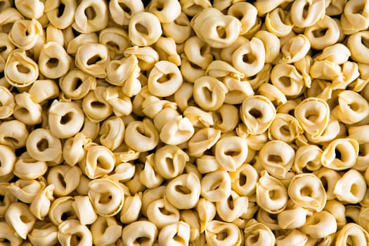 Background texture of Italian tortellini pasta with its traditional curled shape resembling a belly button or navel, full frame view of a layer surface