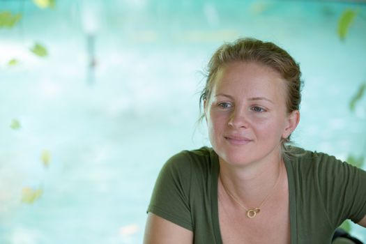 Tranquil moments with a pretty woman gazing ahead with a serene expression and gentle smile against a backdrop of an azure blue pond with copyspace