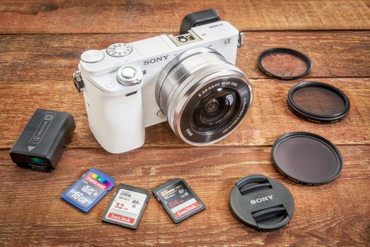 FORT COLLINS, CO, USA, April 17,  2015:  Sony A6000 mirrorless digital camera with a set of filters, memory cards, lens cap and battery on a grunge barn wood table