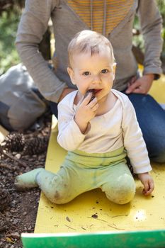 Little boy biting a cone while sitting on a touristic mat on the ground, mother behind the boy