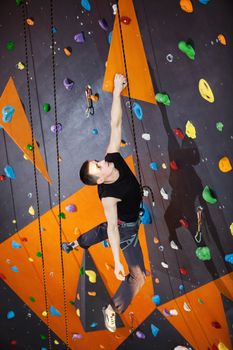 Young man practicing rock-climbing in climbing gym indoors